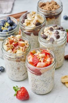 four mason jars filled with overnight oatmeal next to sliced bananas and strawberries