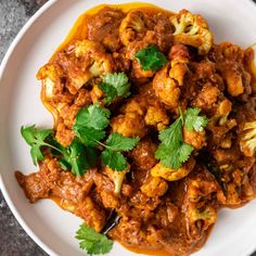 a white plate topped with cauliflower covered in sauce and garnished with cilantro