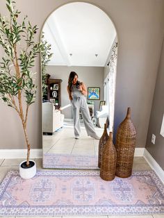 a woman taking a selfie in front of a mirror with a vase on the floor