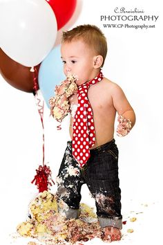 a young boy wearing a red tie and eating cake with balloons in the back ground