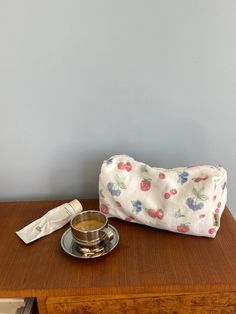 a wooden table topped with a cup and saucer next to a white bag on top of it