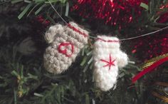 two crocheted mittens hanging from a christmas tree ornament with red and white decorations