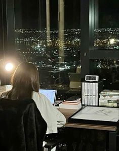 a woman sitting at a desk in front of a window with a laptop computer on it