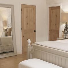 a white bed sitting in a bedroom next to a wooden door and mirror on the wall