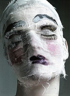 a woman's face is covered in white netting and feathers, with her eyes closed