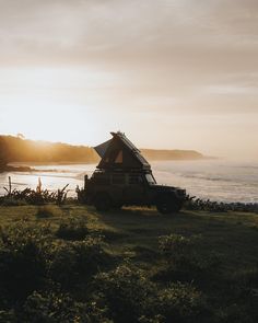 a truck parked on top of a lush green field next to the ocean at sunset