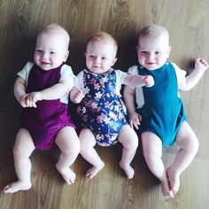 three babies sitting next to each other on top of a wooden floor with their hands in the air