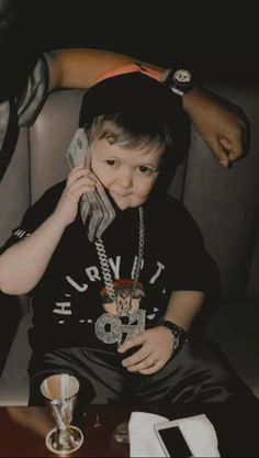 a young boy sitting on a couch talking on a cell phone with his hand over his ear