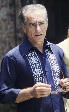 an older man holding a wine glass and looking at the camera while standing next to a woman