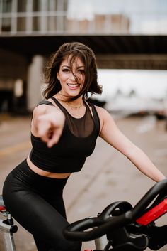 a woman in black top and leggings on a bike pointing at the camera