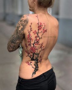 the back of a woman's body with tattoos on it and flowers in bloom