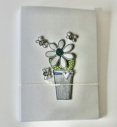 a card with flowers in a pot and bees on the side, sitting on a white surface