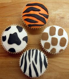 four cupcakes decorated with zebra and giraffe designs on top of a wooden table