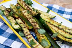 grilled zucchini with herbs on a yellow and white tray sitting on a blue checkered tablecloth