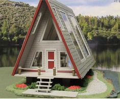 a model house with a red door and windows on the roof is in front of a body of water