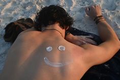 a man laying in the sand with his face painted like a smiley face on his chest