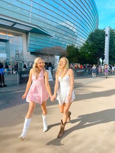 two women in short dresses and cowboy boots holding hands