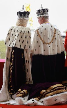 two men dressed in costumes sitting next to each other on a red bench with one man wearing a crown