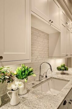 a kitchen with white cabinets and marble counter tops, along with a sink in the center