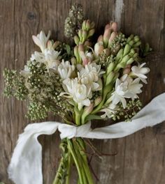 a bouquet of white flowers tied to a wooden wall with a ribbon around the stems