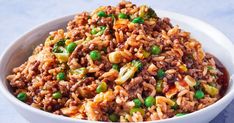 a white bowl filled with rice and vegetables on top of a blue tablecloth next to a fork