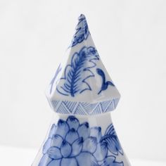 a blue and white ceramic christmas tree with flowers on it's sides, in front of a white background