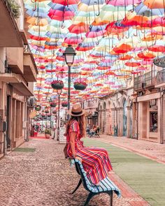 a woman sitting on top of a bench under an umbrella covered street light next to buildings