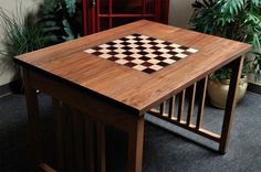 a wooden table with a chess board on it in front of some potted plants