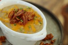 a white bowl filled with soup on top of a metal tray covered in bacon and cheese