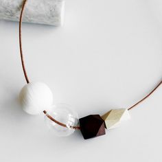 a necklace made with wood and glass beads on a white surface next to a roll of fabric