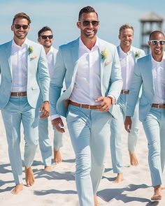 a group of men in light blue suits walking on the beach with one man wearing sunglasses