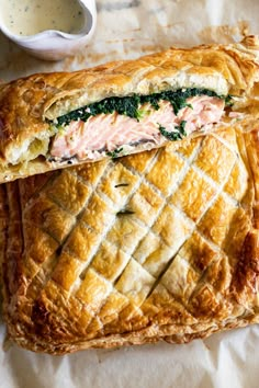 a pastry with salmon and spinach in it next to a cup of sauce on a table