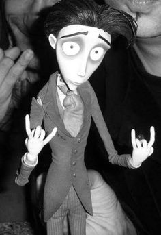 a black and white photo of a doll with two fingers up in the air next to a man's face