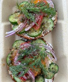 two sandwiches with cucumbers, onions and dill sprouts on them