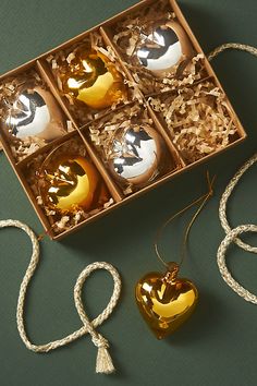 four gold and silver ornaments in a box on a green surface with white string around them