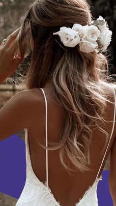 a woman with long hair wearing a white dress and flowers in her hair is looking back