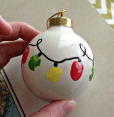 a hand holding a white ornament with christmas lights on it's side