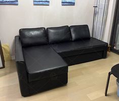 a black leather couch sitting on top of a hard wood floor next to a window