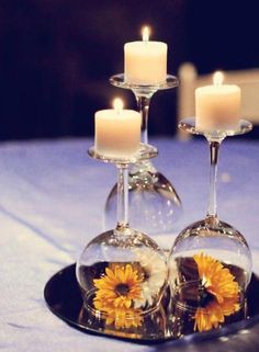 two wine glasses with sunflowers in them are sitting on a table next to candles