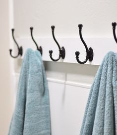 towels are hanging on the hooks in front of a white wall with black handles and an open towel rack