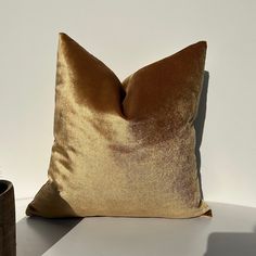 a gold pillow sitting on top of a table next to a vase and potted plant