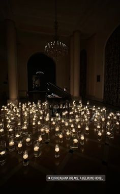 many lit candles are placed on the floor in front of a piano and chandelier