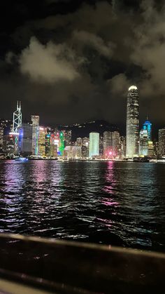 the city skyline is lit up at night from across the water with clouds in the sky