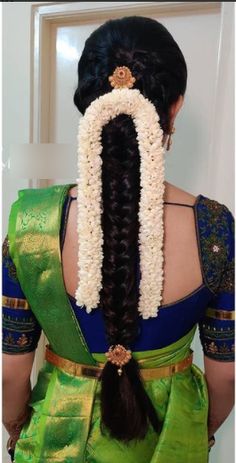 the back of a woman's head wearing a green saree with flowers in her hair