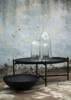 two glass vases sitting on top of a table next to a bowl and bottle