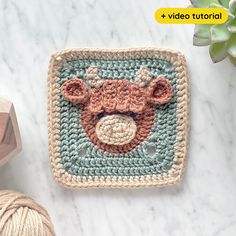 a crocheted square with a teddy bear on it and yarn next to it