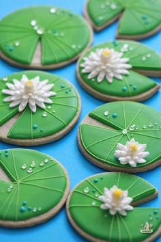 cookies decorated with green leaves and white flowers on a blue tablecloth are arranged in the shape of water lilies