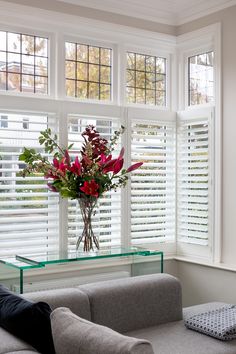 a man sitting on a couch in front of a window with white shutters and flowers