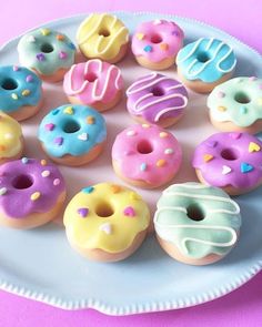 a white plate topped with lots of different donuts on top of a pink table