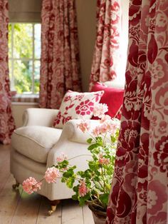 a living room with red and white curtains on the window sill, pink flowers in vase